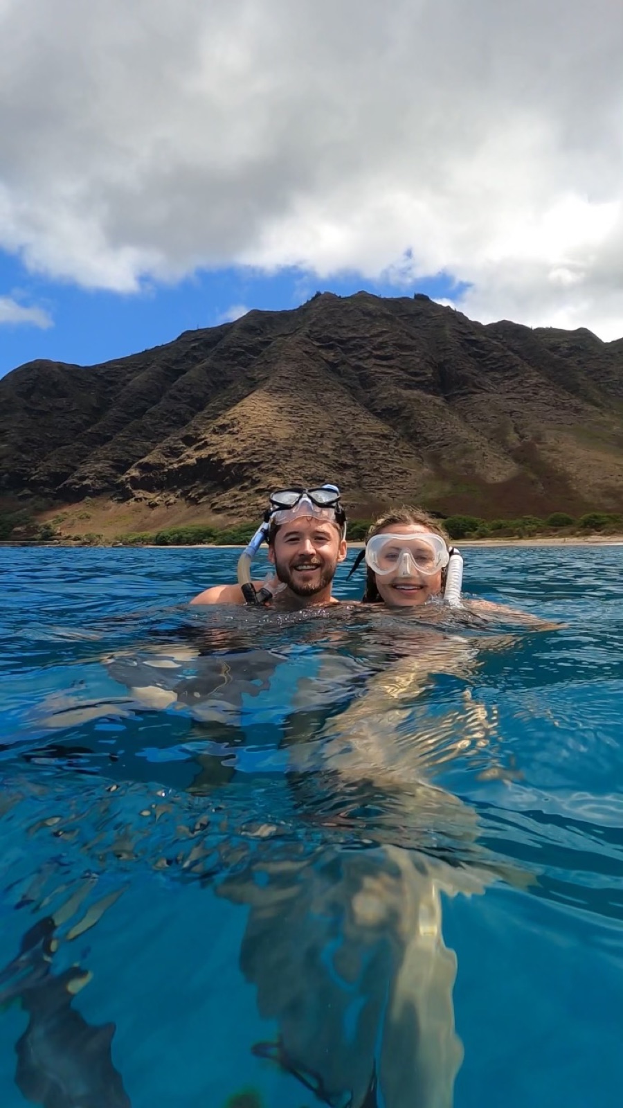 Aidan snorkeling in the ocean with her fiancé, mountain in the background